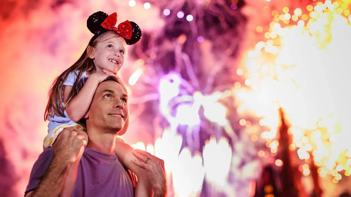 daughter sitting on father's shoulders with fireworks in background